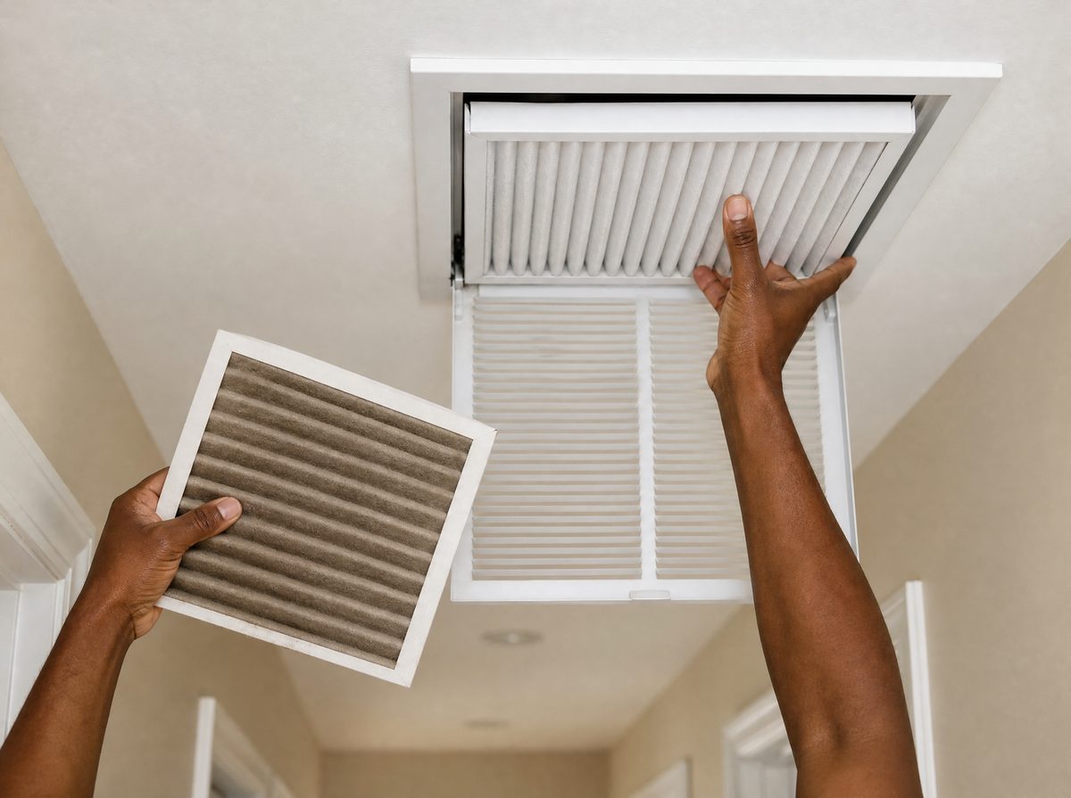 Hands swapping a dusty pleated air filter for a fresh one at a ceiling return vent