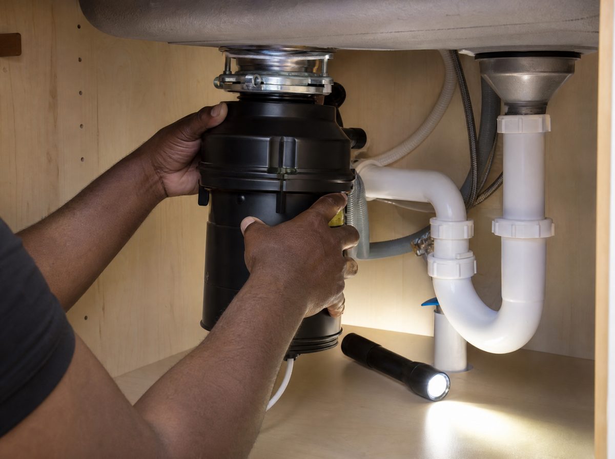 A crew member fitting a new garbage disposal under a kitchen sink